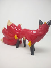Glossy ceramic sculpture of a red fox with a large tail, composed of 9 different smaller tails. The fox has a small golden horn and some gold flames come of its body.