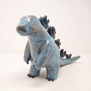 Ceramic sculpture of a brown and blue abstract Godzilla figure, with abstract dark blue spikes on its back, no facial features, and one arm extended out in front.