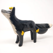 Ceramic sculpture of a black fox with white chest and tail tips. The fox has 3 tails and small golden flames coming off its head and legs.
