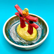 Ceramic sculpture of a red gate with a small orange citrus on top, within a ceramic bowl.