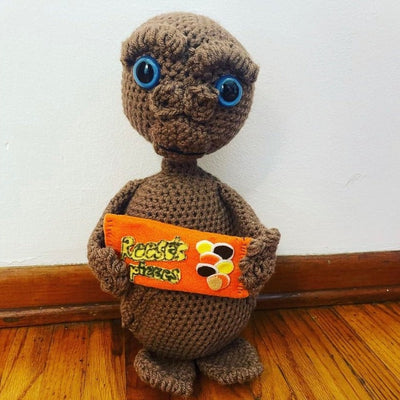 Crochet sculpture of ET, holding a pack of knitted Reese's Pieces.