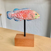 Sculpture of a spotted grouper fish, with bright red dots, blue coloring on its tail/fins and a light green coloring around the face.