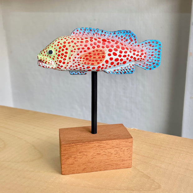 Sculpture of a spotted grouper fish, with bright red dots, blue coloring on its tail/fins and a light green coloring around the face.