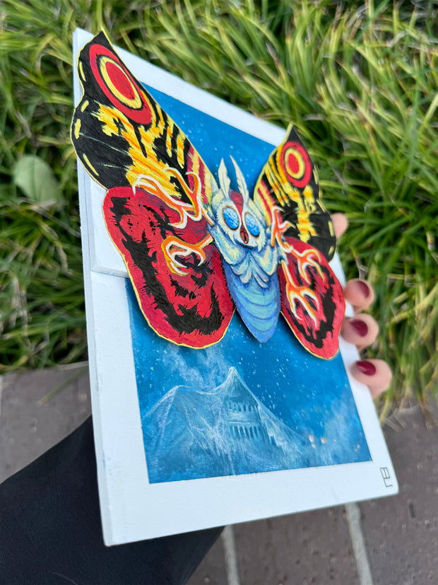 Painting of Mothra, with bright red, yellow and black wings and many clawed feet coming out of its body. It flies over a blue town, covered in a thin white web.