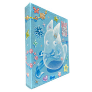 Painting on blue canvas of a see through small Totoro like spirit. On the surface behind it are many trinkets, stars and heart shaped items with a sheen to them. Sides of panel are painted.