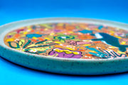 Round ceramic plate with many colorful drawings all along the main face of the plate with themes of underwater characters and creatures with seaweed and corals.