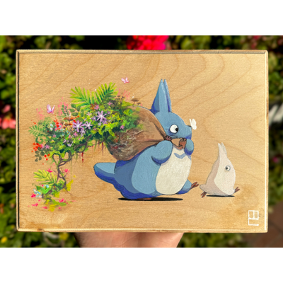 Painting on exposed wooden panel of a blue Chibi Totoro, holding a brown sack over its shoulder. Lush greenery and flowers burst from the bag behind.