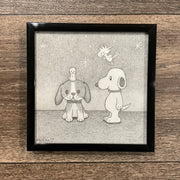 Pencil sketch of a beagle sitting with a chick sitting atop its head. Standing next to them is Snoopy, who smiles and Woodstock flies behind him. Piece is framed.