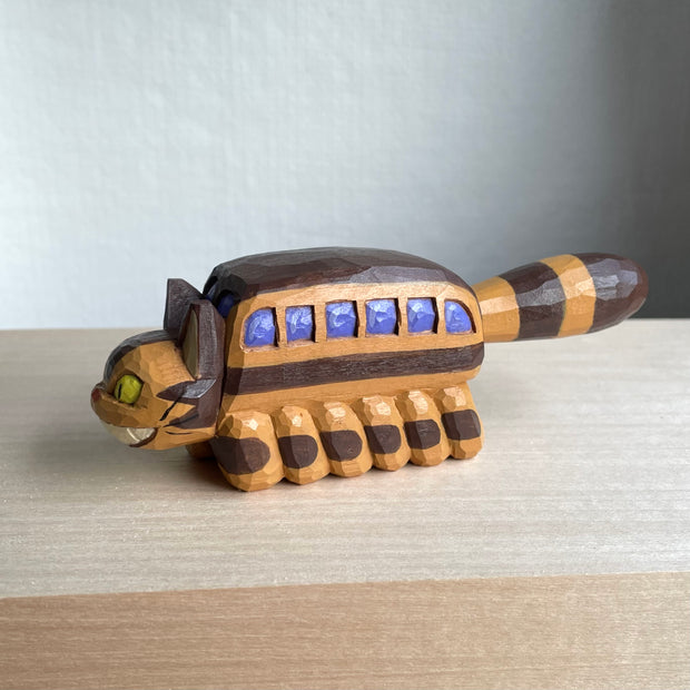Whittled wooden sculpture of a cat shaped like a bus from My Neighbor Totoro. Its tail sticks straight out and it has a smiling face.