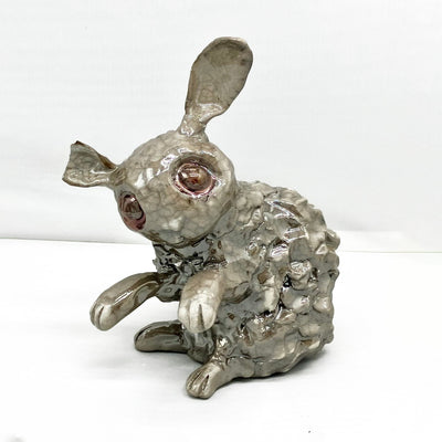 Ceramic gray bunny with textured fur and large copper colored eyes. Its sitting and has its front paws raised.