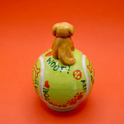Ceramic sculpture of a small brown dog smiling and sitting atop a large tennis ball, with affirmations written on it with cute dog themed doodles.