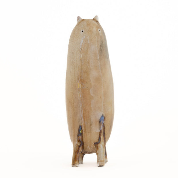 Ceramic sculpture of a tall brown character with tiny ears and eyes and stubby legs, no arms.