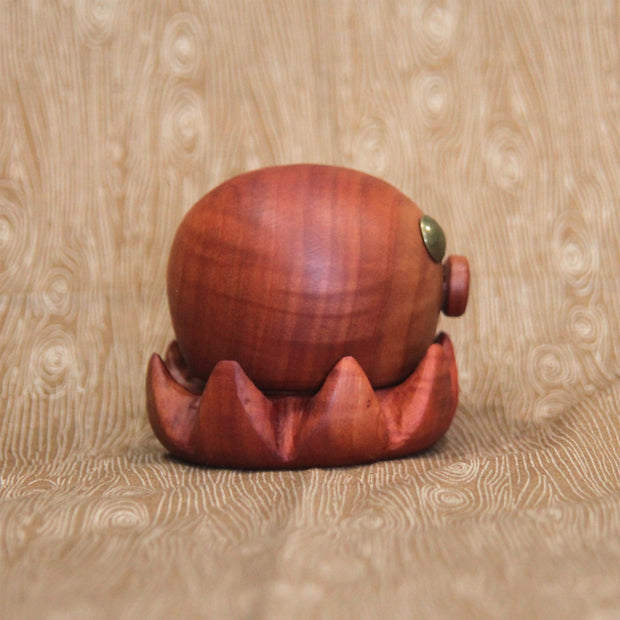 Wooden sculpture of a small octopus, with shiny metal eyes and an "o" shaped mouth. Its tentacles curl up towards itself.
