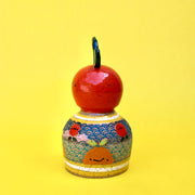 Ceramic sculpture of a bright colored orange, acting as a knob handle atop of an upside down dome shape. The dome has paintings of semi circle patterns and other oranges.