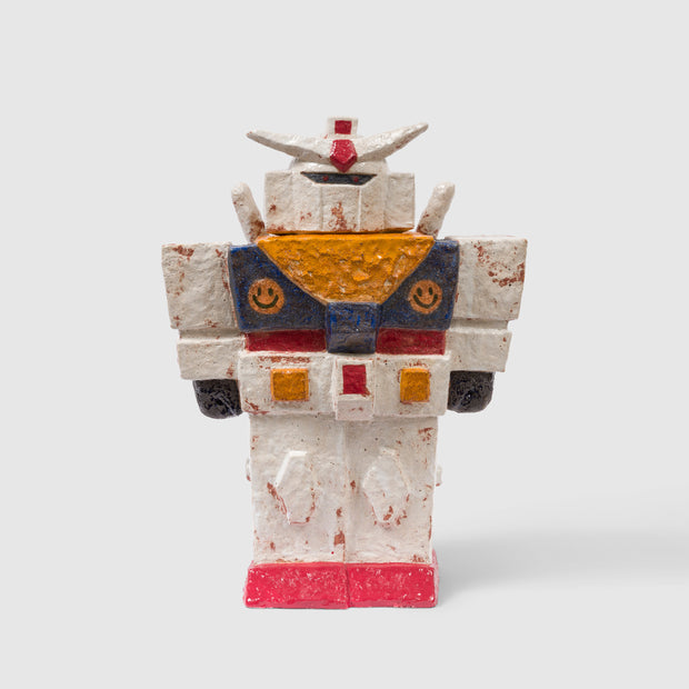 Stoneware ceramic sculpture of a white gundam robot with classic body shapes and white, red, blue and yellow coloring. It has 2 smiley faces on its chest.