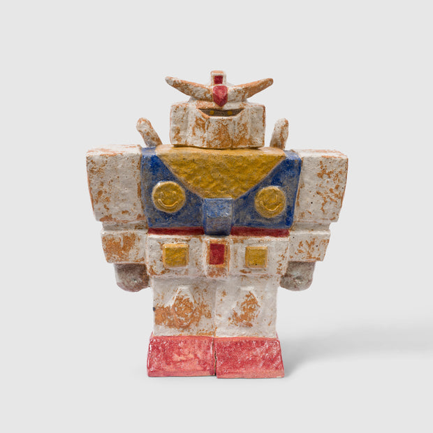 Stoneware sculpture of a large, wide shouldered Gundam robot with classic white, red, yellow and blue coloring. It is slightly worn looking, as if buried in dirt with residue still on it.