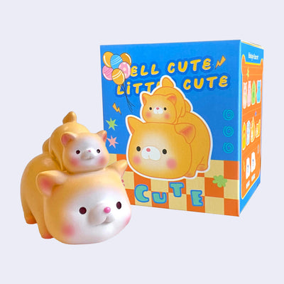 Small cute figurine of 2 orange cats, one larger and one smaller stacked atop the other. It stands next to its product packaging.