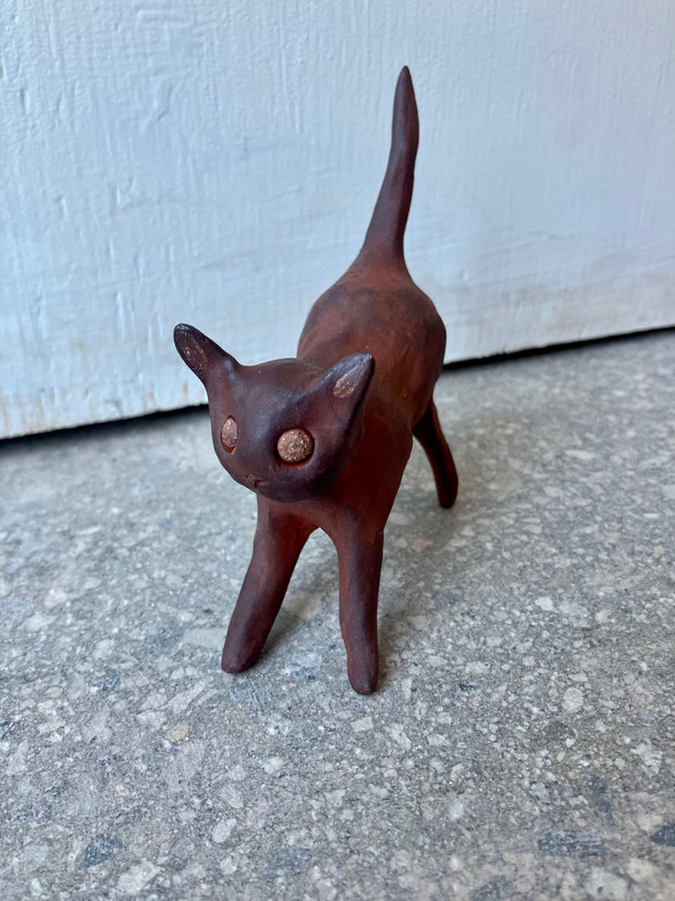 Burnt orange colored sculpture of one large cat with gold sparkly eyes.