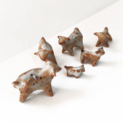 Set of 6 small ceramic dogs, without any facial features and minimal body definition. They are white and brown speckled and have dots on them.