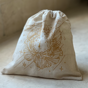 Closed cream colored linen bag with a graphic of a illustrated moonflower on the front in gold ink.