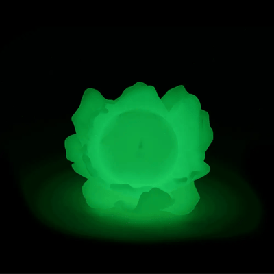 Glow in the dark colored vinyl figure of a round full moon with a small minimalistic face. It sits within a series of flower petals, as if it is the pistil of the flower. Gif goes from lights on, to lights off to show the glow of the figure.