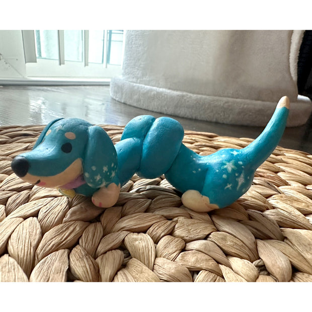 Sculpture of a long blue dog, similar to a Dachshund with its body twisted around like a tangled slinky. It has small white stars on it.