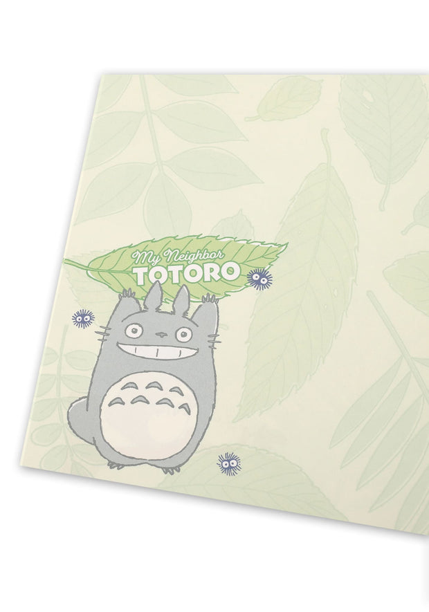 Notebook interior with green leaf patterned pages and Totoro holding a leaf over his head with small dust sprites around.