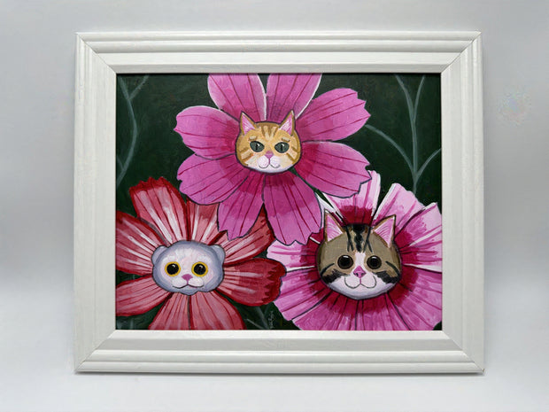 Painting of 3 pink flowers with cat heads in the center of each. One cat is white, the other is orange and the last is a brown striped cat. Framed in white wooden frame.