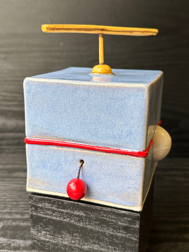 Back view of ceramic cube designed to look like Doreamon, with a propeller coming out atop his head and a red circle attached to a string for a tail.