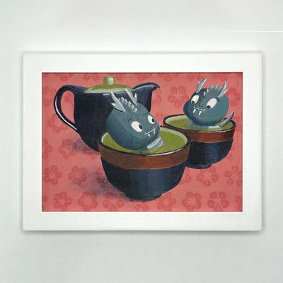 Framed illustration of a pair of 2 small cartoon dragons, sitting in a cup of green tea. Behind them is a black tea pot. Background is reddish pink with a painted flower pattern.