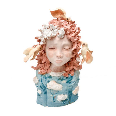 Ceramic sculpture of a girl with closed eyes and textured orange hair. Her eyes are closed and birds are feeding on her hair.