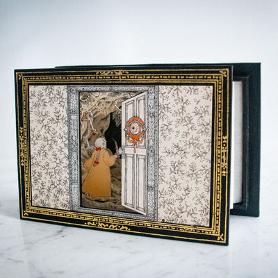 Accordion style diorama of a an open door, with a woman in a orange night gown holding up a candle and walking through many layers of whimsical forest. Border of the piece is gold and black.