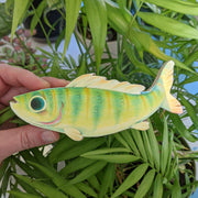 A hand holds a 5.5" long illustration of a green fish. It has striping down its body, large blue eyes, a wavy top fin, and a friendly, excited smile. 