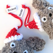 Close up of crocheted Totoro ornaments, with small red Santa hats hanging on one of their ears.