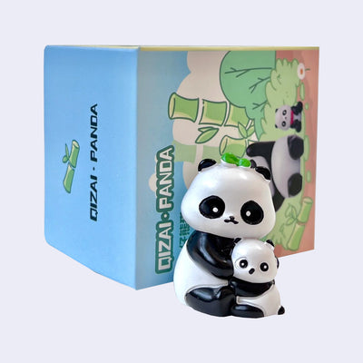 Small plastic figurine of a panda, hugging a baby panda. It sits in front of its product packaging.