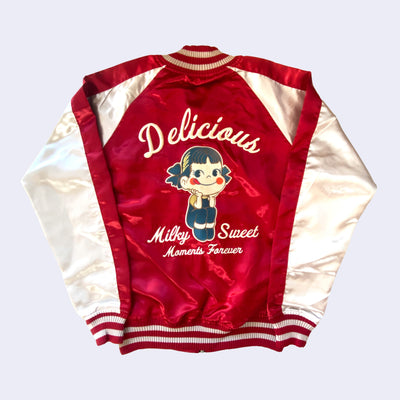 Shiny polyester bomber jacket with red body and white sleeves. Back has a large embroidery of Peko Chan, sitting with her elbows on her knees and smiling. Text around her reads "Delicious Milk Sweet Moments Forever"