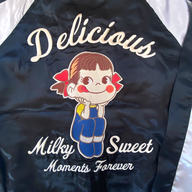 Shiny polyester bomber jacket with black body and white sleeves. Back has a large embroidery of Peko Chan, sitting with her elbows on her knees and smiling. Text around her reads "Delicious Milk Sweet Moments Forever"