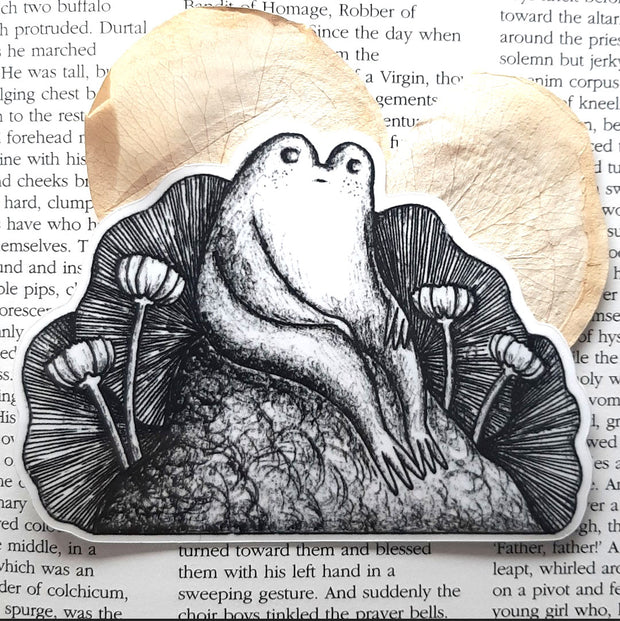 Black and white sticker of a pensive frog sitting on a rock.