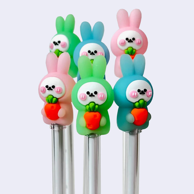 6 pens topped with small plastic figures of rabbits holding large carrots to their chests. Rabbits have cute pink cheeks and are either blue, green or pink.