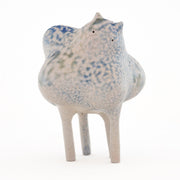 Ceramic sculpture of a character with a lumpy spotted body, tall thin legs, and small eyes and ears.