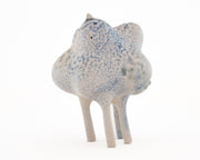 Ceramic sculpture of a character with a lumpy spotted body, tall thin legs, and small eyes and ears.