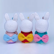 Back view of 3 crocheted white bunnies, standing up wearing different colored kimonos with large bows in the back. Kimono colors are: pink, red, and turquoise.