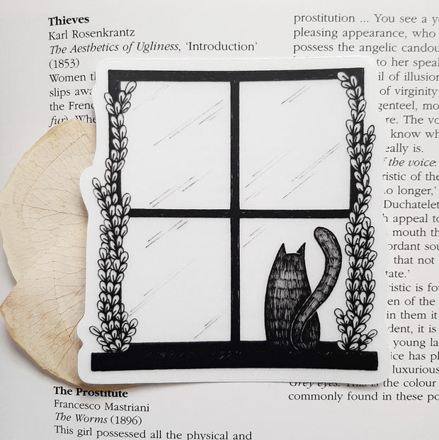 Black and white sticker of a window pane and a small cat sitting and looking out the window.
