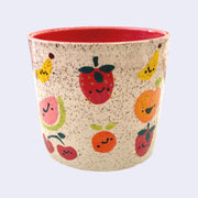 Ceramic planter with spotted finishing and an earthy cream exterior and pinkish red interior. On the outside are painted on cartoon style assorted fruits, with simple expressions.