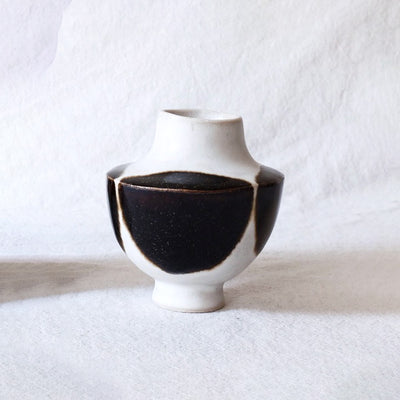 Small sculpture of a white vase with large black circles around it.