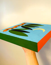 Solid color painting on panel of a blue background. A simply painted orange and black snake is at the bottom between blades of tall grass. A simplistic crescent moon hangs overhead.