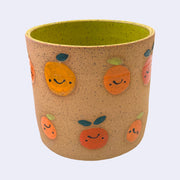 Ceramic planter with spotted finishing and an earthy brown exterior and lime green interior. On the outside are painted on cartoon style citrus fruits, with simple expressions.