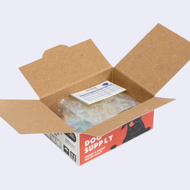 Open box of miniature stickers, made to resemble a shipping box with bubble wrap around the product and a small invoice. Exterior of box looks like realistic dog supply box.