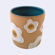 Ceramic planter with spotted finishing and an earthy brown exterior and teal interior. On the outside are painted on cartoon style eggs, with simple expressions.