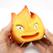 Whittled wooden sculpture of a flickering flame, with cute cartoon eyes and an open mouth smile. Painted like Calcifer from Howl's Moving Castle.